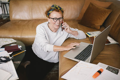 Happy senior woman talking on mobile phone and using laptop at home