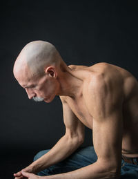 Shirtless mature man sitting against black background
