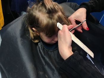 Cropped hands of barber cutting girl hair