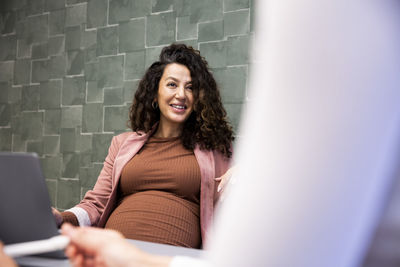 Smiling pregnant businesswoman talking with female colleague in office