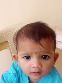 Close-up portrait of baby boy sitting on chair against wall