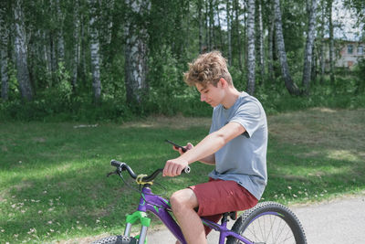 Curly teenager boy riding a bike or bicycle and texting. teenager looking at smartphone