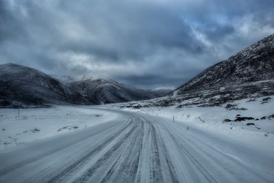 Snow covered road by mountain against sky