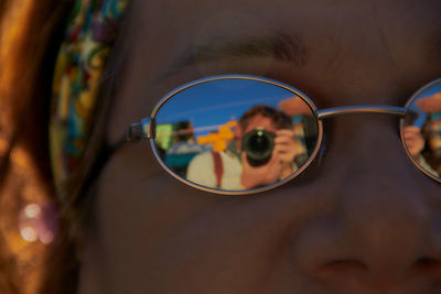 Close-up portrait of young woman with reflection of man in sunglasses