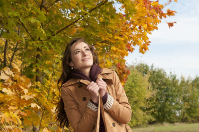 Thoughtful woman smiling while standing at park during autumn