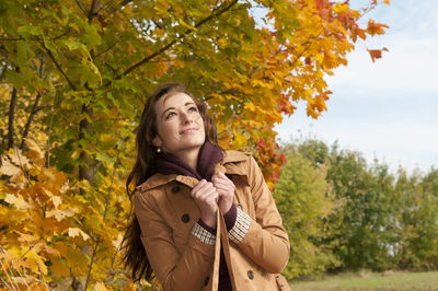 Woman wearing coat standing against trees in park during autumn
