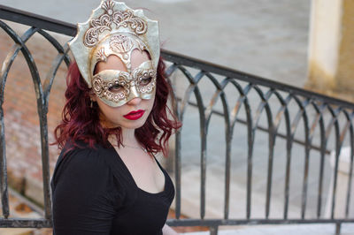 Young woman wearing mask by railing during carnival