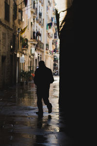 Rear view of silhouette man walking on street amidst buildings