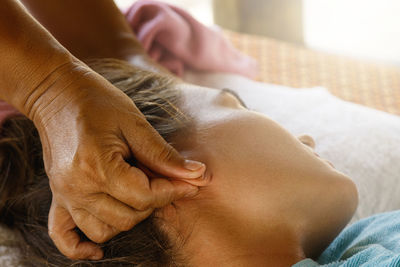 Cropped hand of massage therapist massaging woman ears at spa