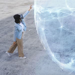 Teenage girl with virtual reality headset touching blue glowing sphere on footpath