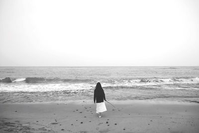 Rear view of woman walking at beach against clear sky