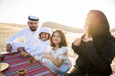 Happy family having tea on carpet at desert