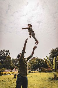 Father throwing son in air while standing at park