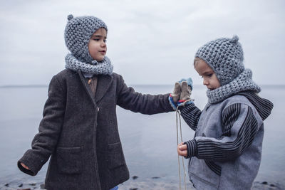 Girl in knitted grey hat sharing gloves with her frozen brother