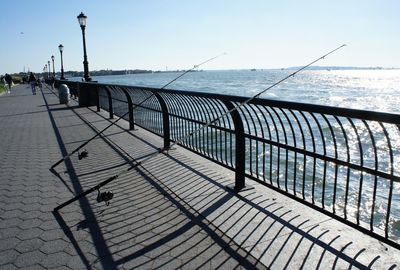 Empty bench on pier by sea against clear sky