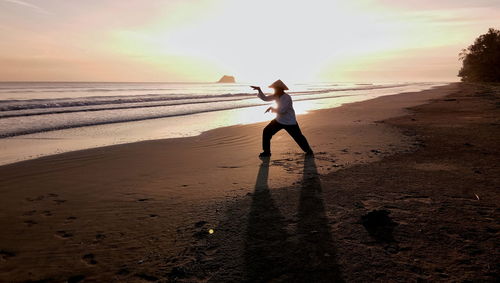 Woman standing on beach against sky during sunset