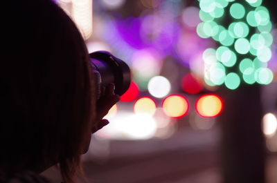 Rear view of photographer photographing illuminated city at night