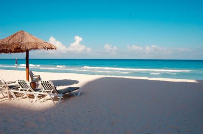 Lounge chairs on beach by sea against sky