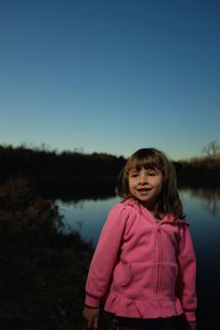 Smiling cute girl standing against lake during sunset
