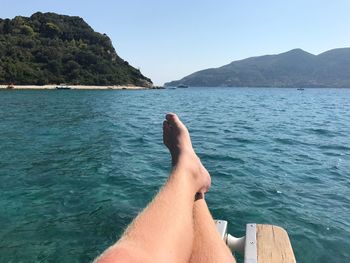 Low section of man in sea against clear sky