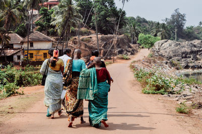 Rear view of people walking on dirt road