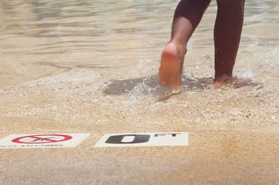 Low section of woman walking on warning sign at poolside