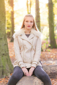 Portrait of young beautiful woman sitting on fallen tree trunk in forest