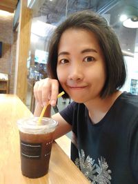 Portrait of young woman drinking glass on table