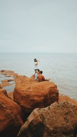 Man on rock at beach against sky