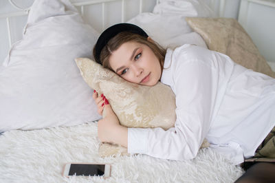 Upset girl is lying on the bed hugging a pillow next to the phone