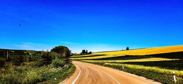 Road amidst field against clear blue sky