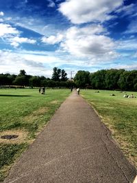 Footpath in park against cloudy sky
