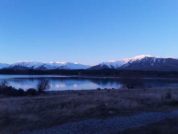 Scenic view of lake and snowcapped mountains against clear blue sky