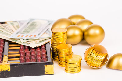 Close-up of abacus with coins and golden eggs on white background