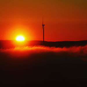 Silhouette of wind turbine against orange sky