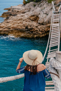 Rear view of young woman standing on old rope bridge over sea cove