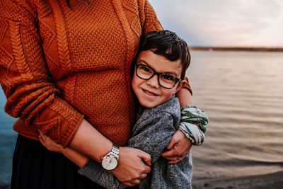 Happy young boy hugging mom near a lake on a autumn evening