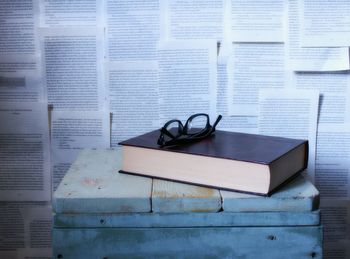 Closed book and eyeglass on table against pages