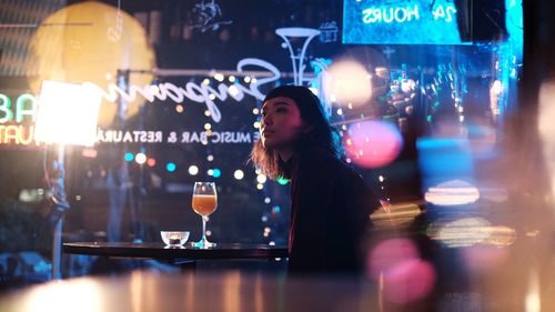 Reflection of woman in glass on table at night