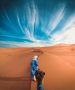 Woman standing on sand dune in desert against sky