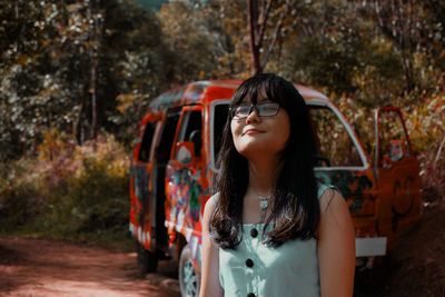 Young woman standing by car at forest