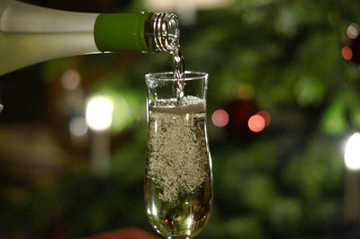 Close-up of champagne pouring in flute against christmas tree