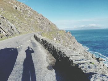 Shadow of person on road by sea against clear sky