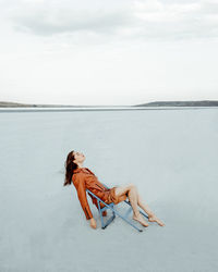 Man sitting on shore at beach against sky