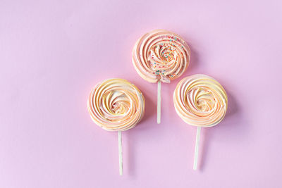 Pink round sweet meringues on a stick with decor lie on a pink background