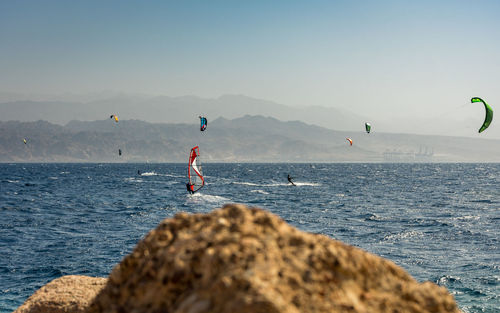 People kitesurfing and windsurfing on sea against clear sky
