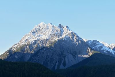 Low angle view of snowcapped mountains against clear blue sky