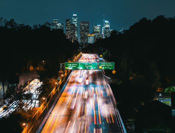 Illuminated city street amidst buildings against sky at night