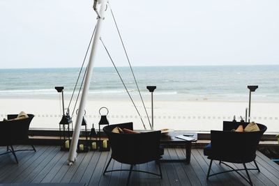 Chairs and table on beach against clear sky