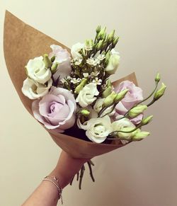 Close-up of woman hand holding bouquet against wall